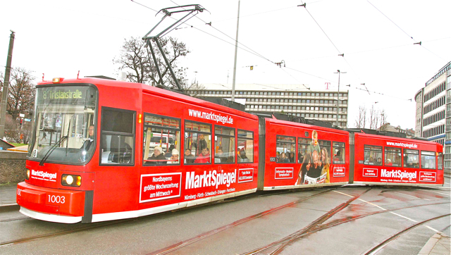 Informativ, modern und sympathisch: so präsentiert sich der MarktSpiegel jede Woche mit einer Geamt-Auflage von über 462.000 Exemplaren. Und seit Montag ist er jetzt in Nürnberg sogar an jedem Tag unterwegs: Das in kräftigen Rottönen gehaltene Logo ziert nämlich die drei Waggons der Straßenbahn HT6N, die auf wechselnden Linien im Stadtgebiet unterwegs ist. Insgesamt 150 Meter Folie sind für die originelle Werbeaktion verwendet worden, das Hauptmotiv zeigt eine junge Familie bei der MarktSpiegel-Lektüre.