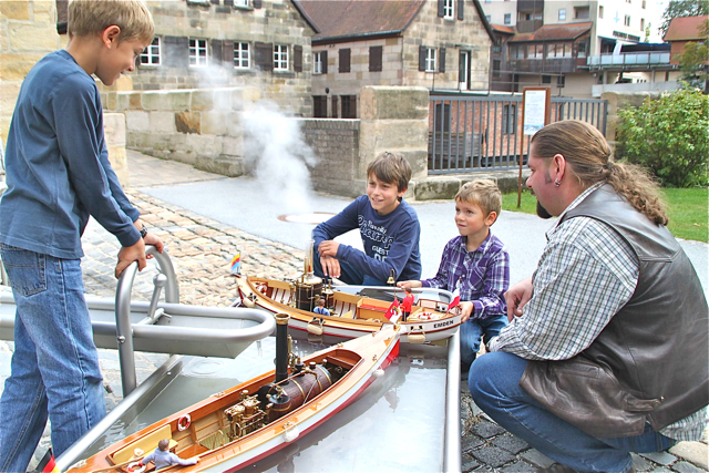 Ben, Nik und Lutz finden den Probelauf zweier Dampfschiffe im Becken des Wasserspielplatzes im Industriemuseum sehr interessant. Die Dampfwolke entsteigt dem Schlot mit einem schrillen Pfeifen.