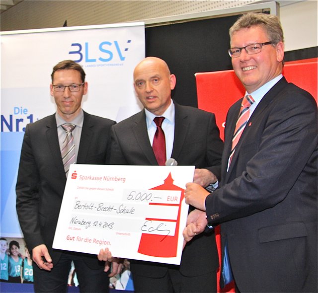 Olympionicke Andreas Dittmer (l.), Deutscher Sparkassen- und Giroverband, und Dr. Matthias Everding (r.), Vorstandsvorsitzender Sparkasse Nürnberg, übergeben Oberstudiendirektor Dr. Harald Schmidt einen Scheck.