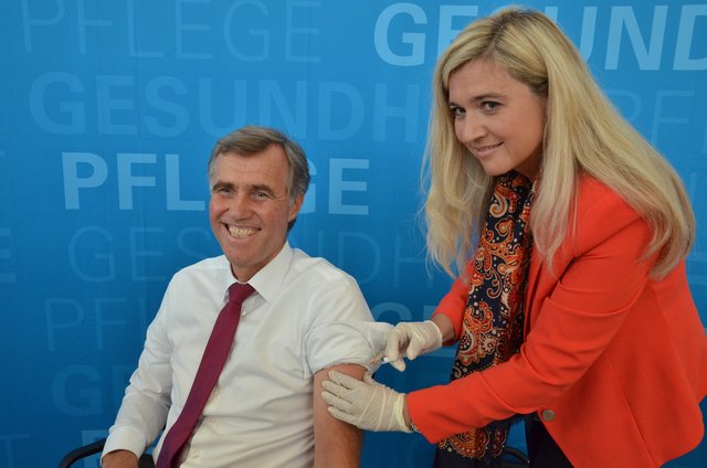 Bayerns Gesundheitsministerin Melanie Huml, die selbst Ärztin ist, impft Dr. Nikolaus Frühwein, den Präsidenten der Bayerischen Gesellschaft für Immun-, Tropenmedizin und Impfwesen e.V. gegen Grippe.