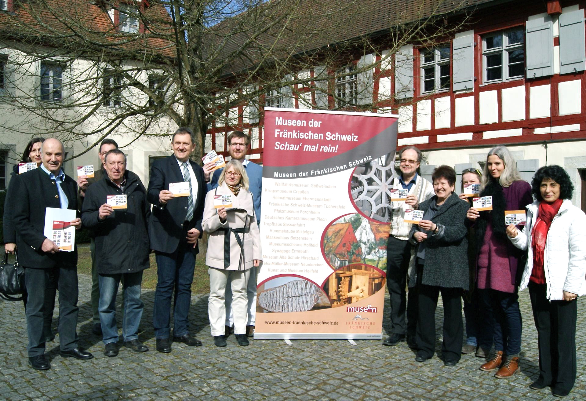 Die Museumsleiter der beteiligten Museen mit dem Bayreuther Landrat Hermann Hübner, Vorsitzender im Zweckverband Fränkische-Schweiz-Museum (5.v.l.), zeigen im Hof des Tüchersfelder Museums die Verbundkarte. Foto: Fränkische Schweiz Museum Tüchersfeld