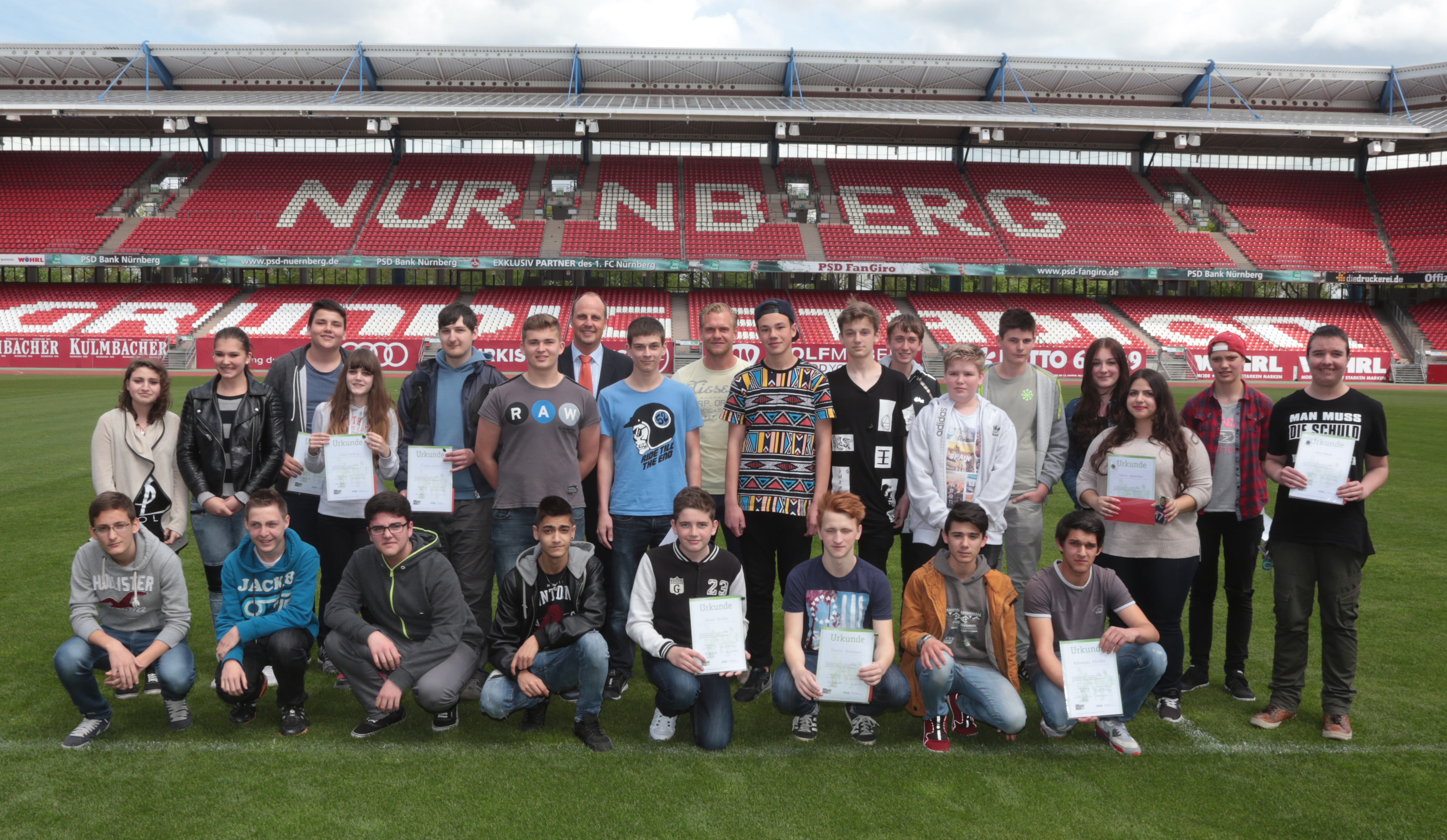 40 Schülerlotsen mit Urkunden beim Gruppenbild mit Andy Wolf und Christian Vogel auf dem Rasen im Grundig-Stadion.