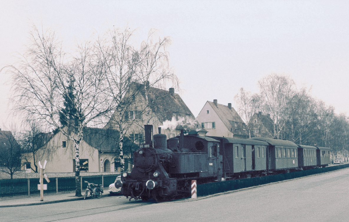 Ein Bild aus längst vergangenen „Seekuh“- Zeiten: 98 805 rumpelt am 04. März 1959 mit ihrem Personenzug durch Erlangen. Das am Straßenrand abgestellte Moped des jungen Fotografen diente lange als fahrbarer Untersatz für die zahlreichen Fotoexkursionen quer durch Deutschland, denen wir die vielen wertvollen Farbaufnahmen aus der Blütezeit der Deutschen Bundesbahn verdanken.