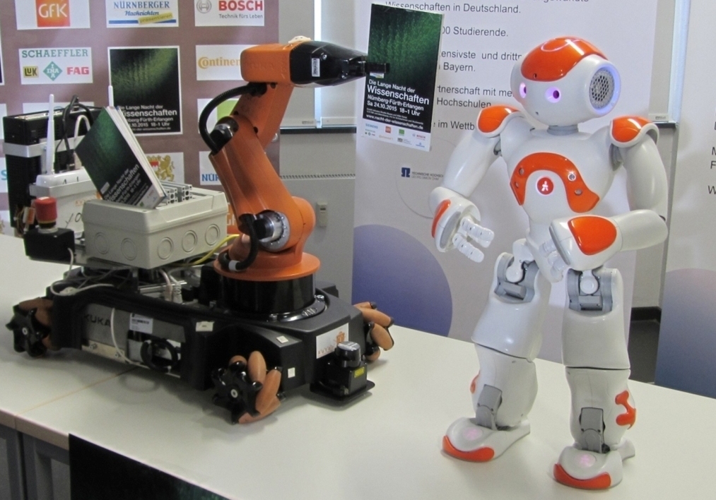 Die sprechenden Roboter NAO Luc und Youbo TH der Universität Erlangen-Nürnberg und der Technischen Hochschule, die sich anlässlich der Langen Nacht voller Vorfreude das Programmheft überreichten.