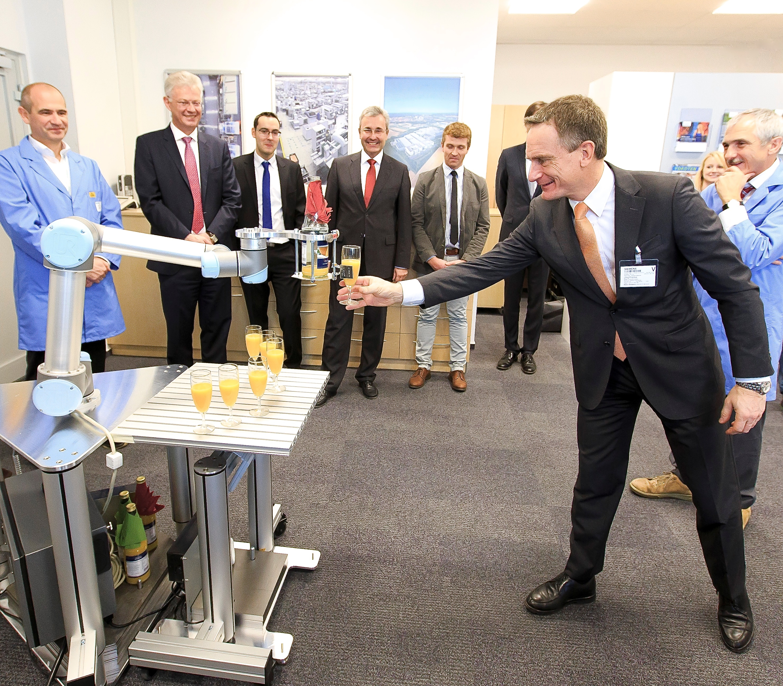 „Robo-Drink“ – sehr zum Wohl! Prof. Dr.-Ing. Jörg Franke, Inhaber des FAPS-Lehrstuhls, nimmt zur Feier des Kooperationsvertrages ein Glas Orangensaft vom Leichtbauroboter entgegen. Foto: Siemens