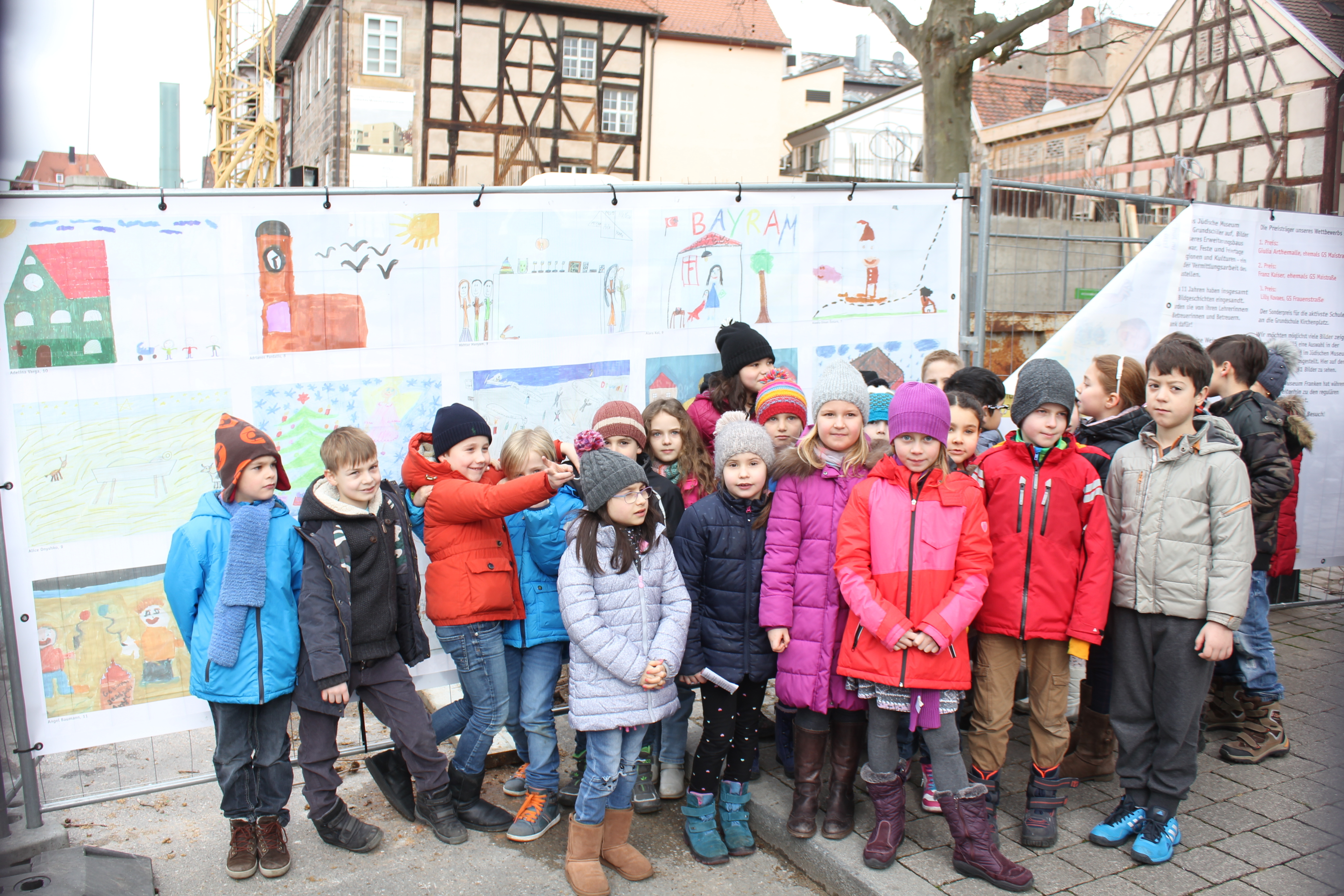 Schülerinnen und Schüler der Grundschule am Kirchenplatz vor ihren Bildern am Bauzaun des Jüdischen Museums. Foto: Ebersberger