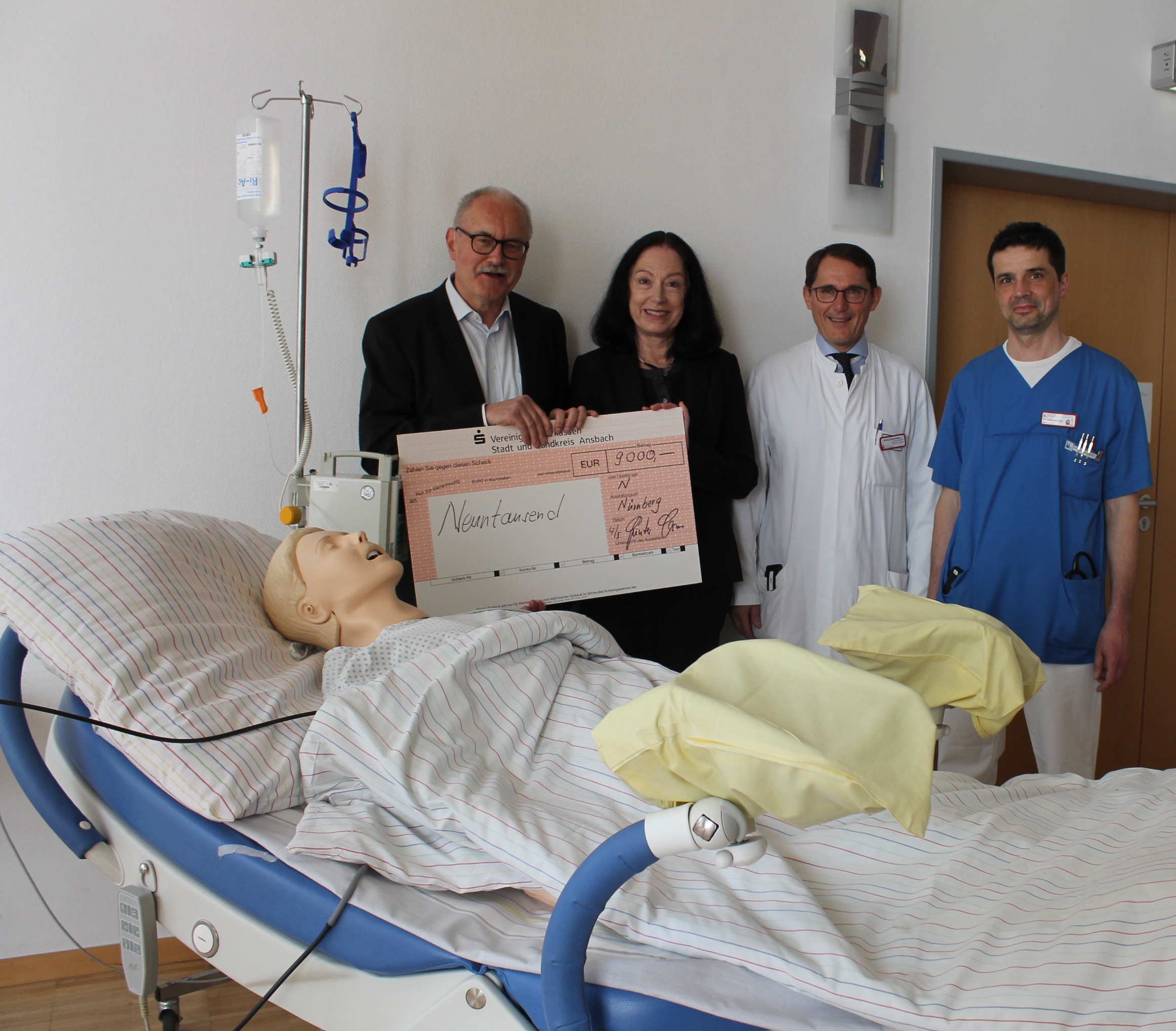 Symbolischer Spendenscheck vor lebensecht wirkender Patientin mit einem wirklichen Geldbetrag. Bei der Übergabe (v.l.) Günter Gloser, Eva Schoenauer, Dr. Franz Kainer und Dr. Bernd Landsleitner.