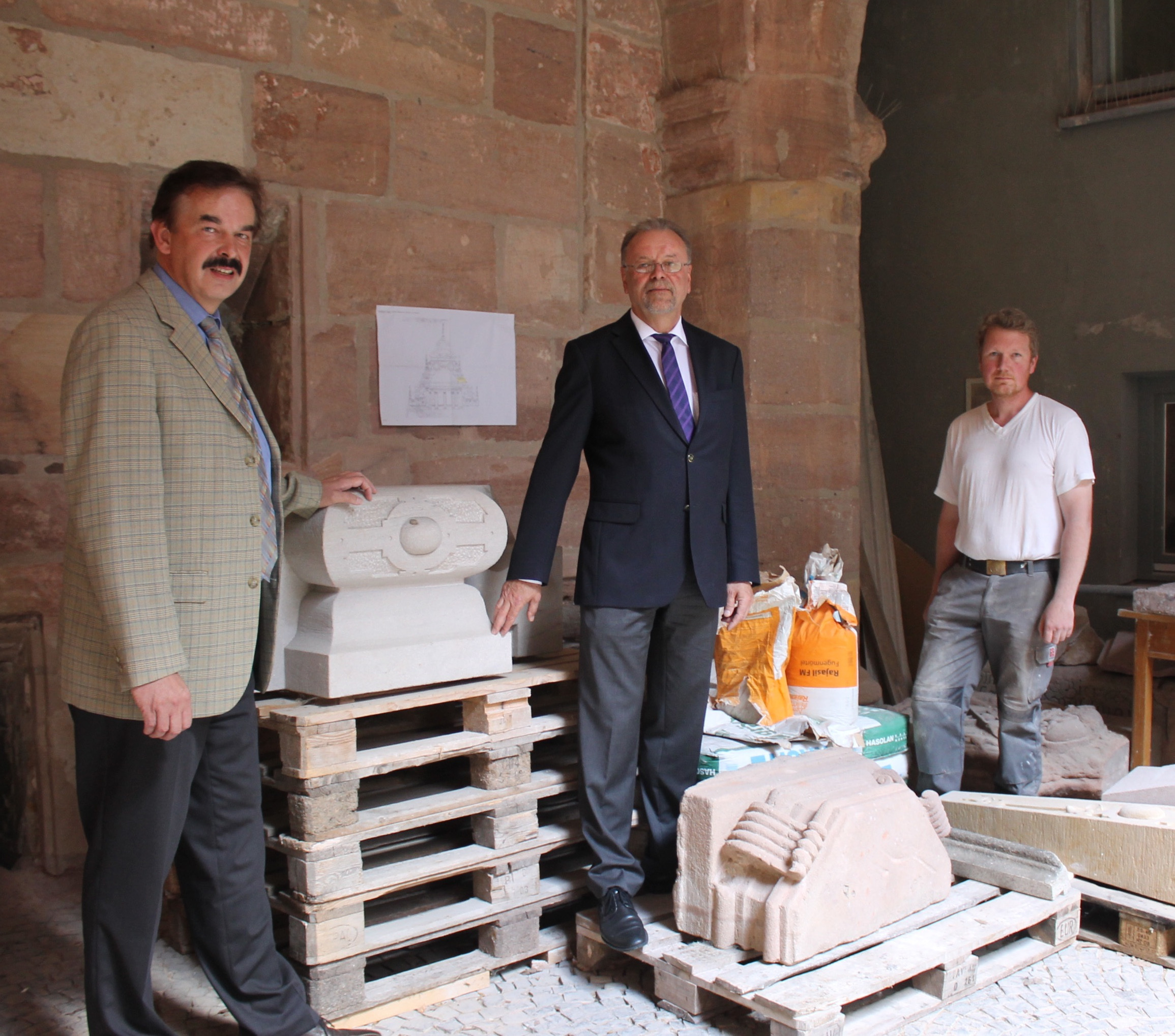 Michael Prymelski (Leiter Zentrale Öffentlichkeitsarbeit Diehl Stiftung), Karl-Heinz Enderle und Steinmetz Harald Pollmann (v.l) begutachten Schmuckelemente, die im Nordgiebel eingebaut werden.