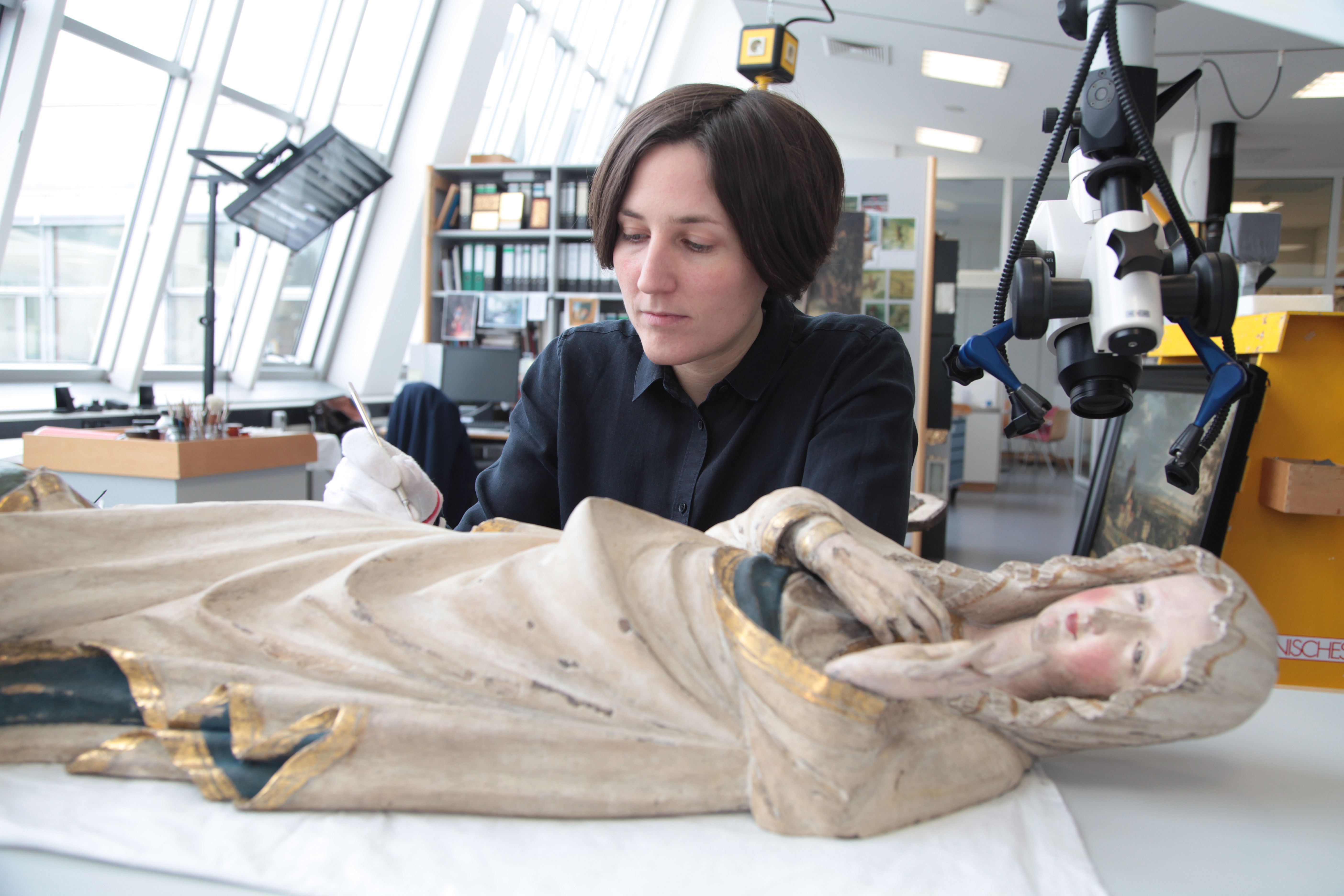 Wibke Ottweiler beugt sich über die Figur der Maria aus der Kreuzigungsgruppe des Deichsler Altars.