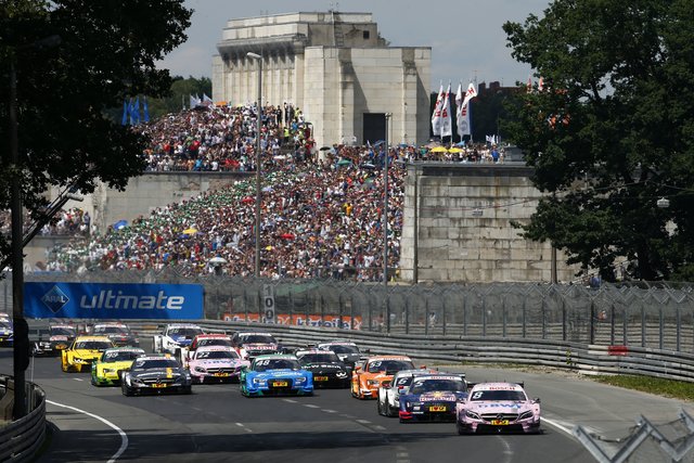 Start zum Rennen! Das Feld jagt vor der alten Steintribüne die Start-/Zielgerade Richtung Grundigkehre (mit 50 km/h die langsamste Kurve) hinunter. Foto: © DTM/HochZwei