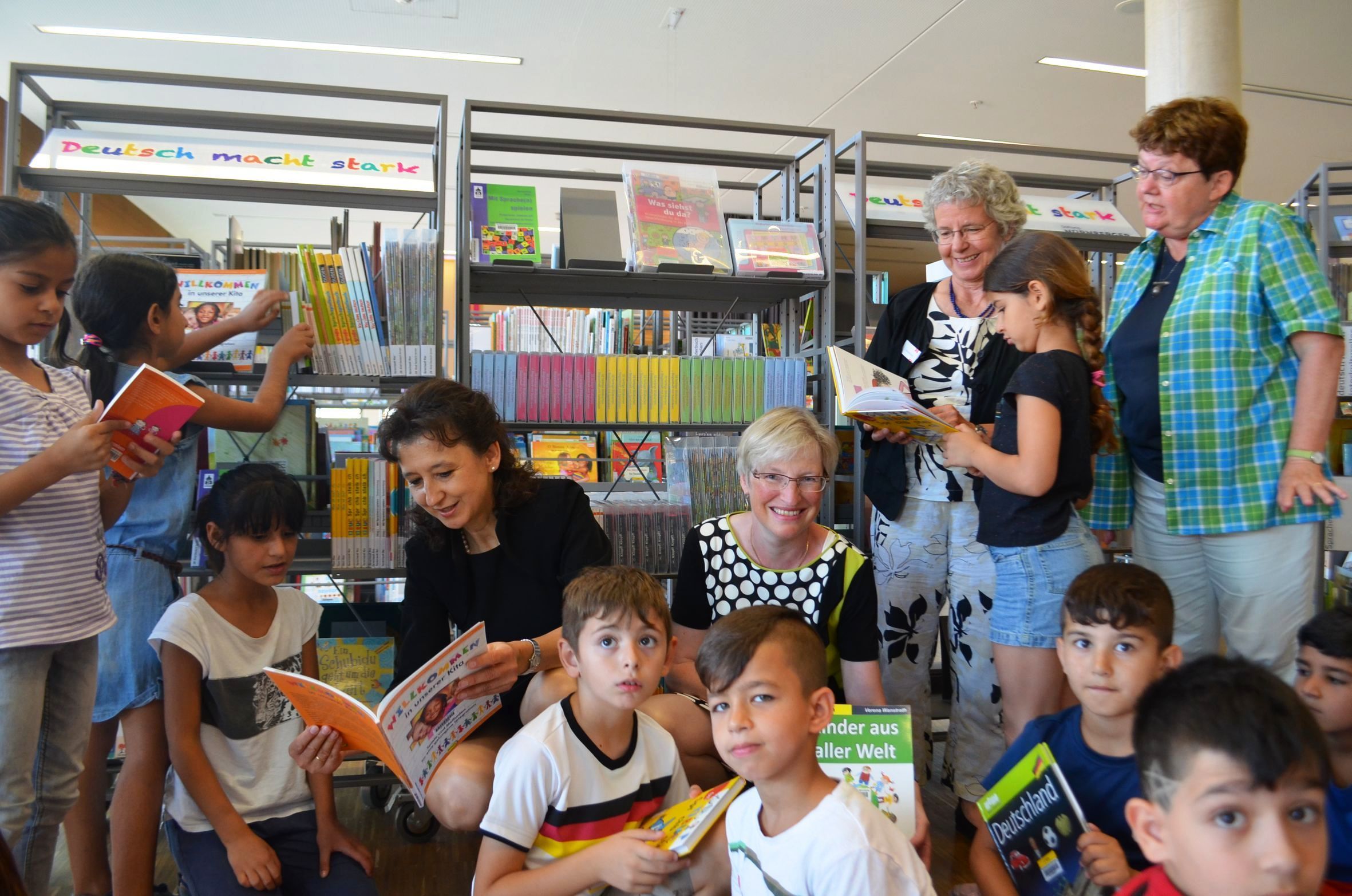 Hannelore Wünsche, Vorsitzende Geschäftsführerin der Stiftung NÜRNBERGER Versicherung, Elisabeth Sträter, Direktorin der Stadtbibliothek im Bildungscampus Nürnberg, Susanne Schneehorst, Mitarbeiterin der Stadtbibliothek Nürnberg (Literatur + Sprache, Interkulturelle Angebote), und Renate Körner, Lehrerin der Klasse 2d der Bartholomäusschule, blättern gemeinsam mit der Schulklasse 2d in den neuen Deutschlernmedien in der Kinderbibliothek.