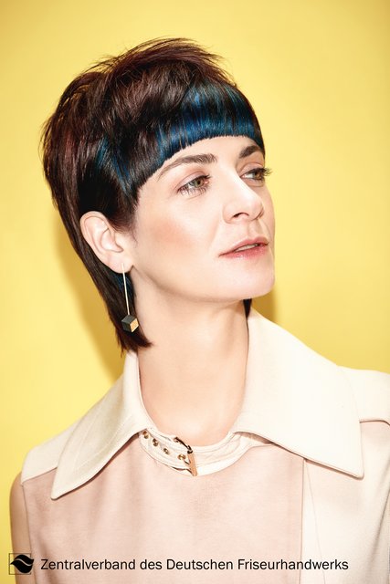 Back to the 80s? Von wegen, der Mullet ist angesagter denn je. Vorne besticht der Schnitt heute durch einen kurzen grafischen Pony, der betont straight gestylt wird. 
Getoppt wird das grafische Element durch Denim-Akzente. Metallisches Violett und Blau schimmert unaufdringlich unter dem satten, braunen Naturton hervor. | Foto: Immo Fuchs, Köln / © Zentralverband Friseurhandwerk, Köln
