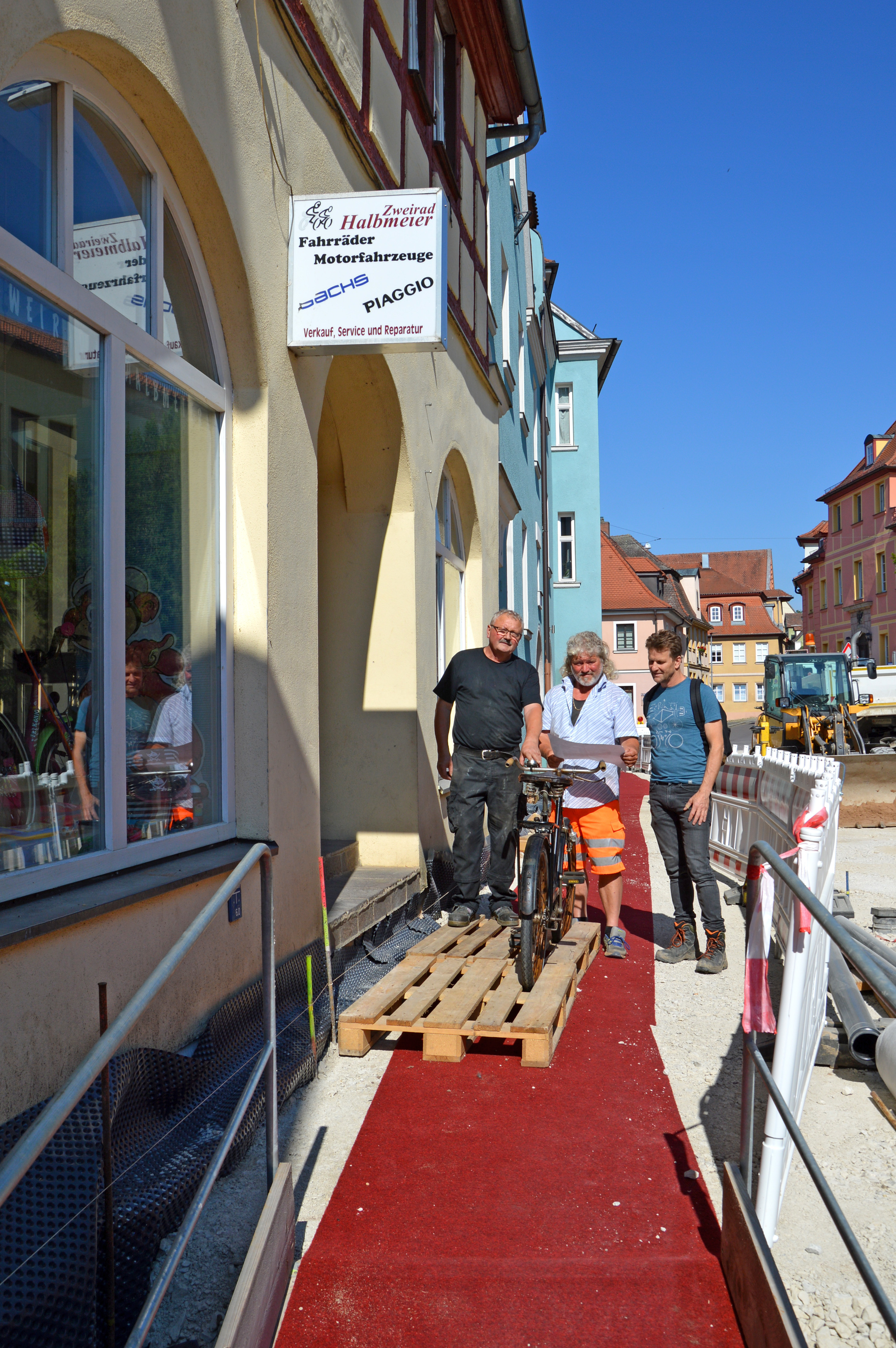 Hans Halbmeier, Polier Volker Rosenthal und Jörg Maier auf dem roten Teppich vor dem Fahrrad-Fachgeschäft.