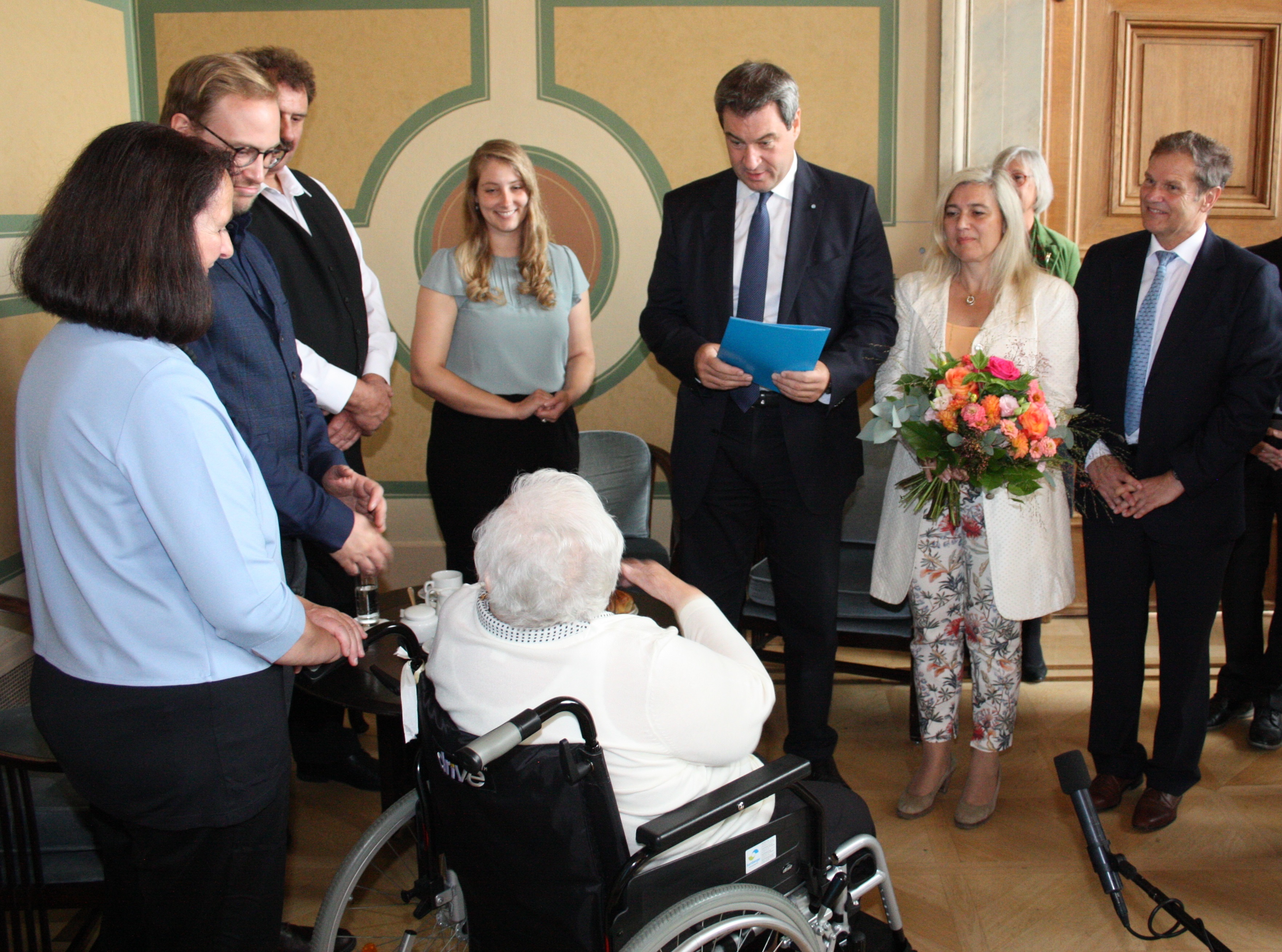 Gemeinsam mit Gesundheitsministerin Melanie Huml und dem Patienten- und Pflegebeauftragten Hermann Imhof übergibt Ministerpräsident Markus Söder einen Bewilligungsbescheid für das Landespflegegeld.