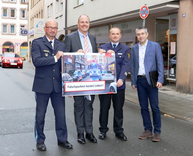 Das Kampagnenplakat (das Motiv dafür wurde in der Jakobsstraße aufgenommen) präsentieren Alfred Stahl (Polizeidirektor), Bürgermeister Christian Vogel, Horst Gillmeier (Wachleiter der Feuerwache 3) und Markus Hübner (Leiter Zweckverband Kommunale Verkehrsüberwachung, Großraum Nürnberg) am gleichen Ort.