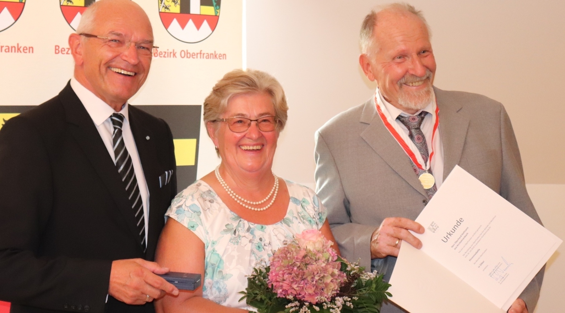 Bezirkstagspräsident Dr. Günther Denzler (links) überreichte die Medaille in Silber an Eberhard Hofmann. Hofmanns Ehefrau bekam einen Blumenstrauß.