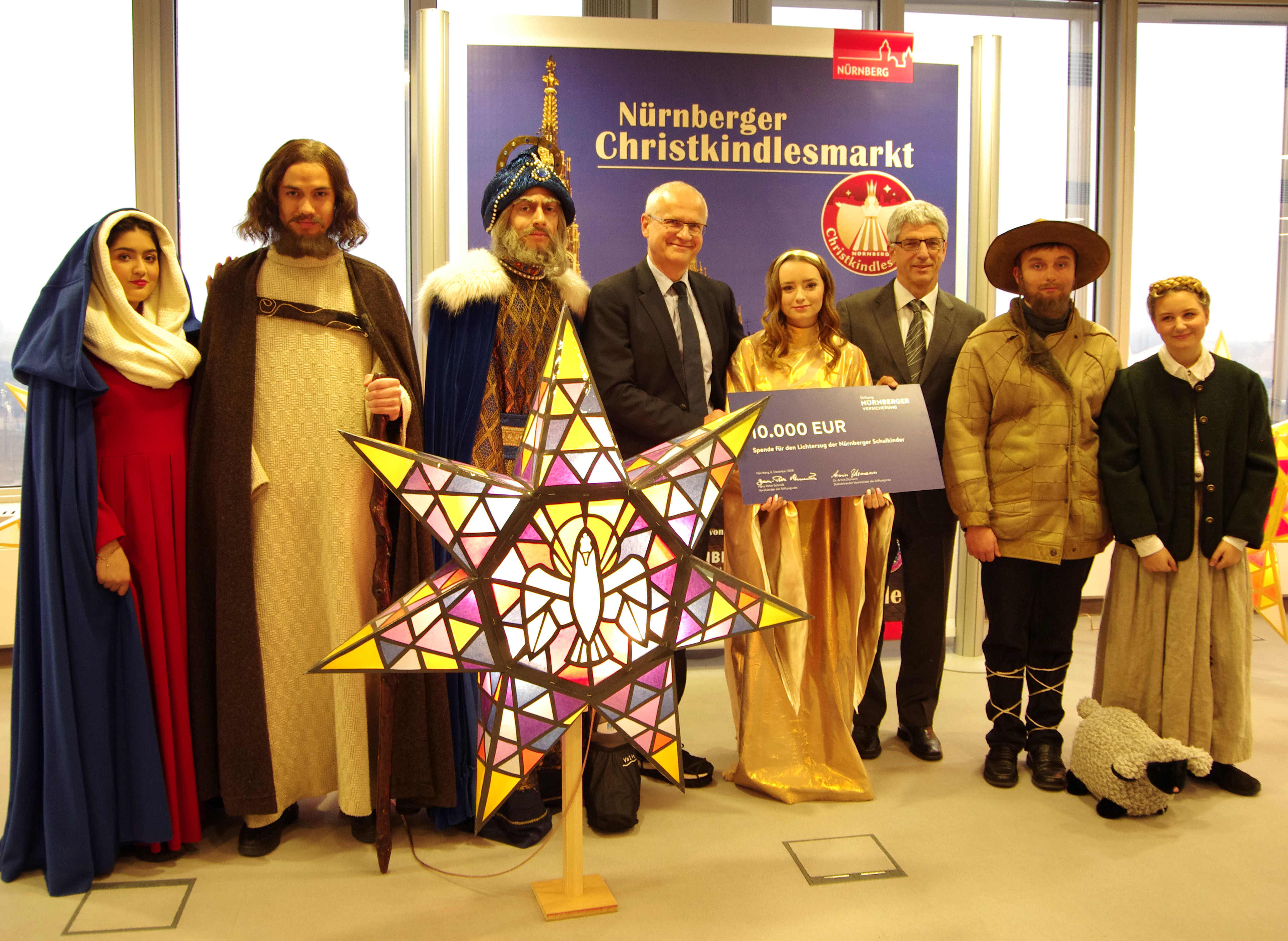 Dr. Klemens Gsell, 3. Bürgermeister der Stadt Nürnberg (4. v.l.), erhielt von Dr. Armin Zitzmann, Vorstandsvorsitzender der NÜRNBERGER Versicherung (3. v.r.), im Beisein der Krippenspieler der Friedrich-Wilhelm-Herschel-Mittelschule den symbolischen Spendenscheck für den Lichterzug der Nürnberger Schulkinder.