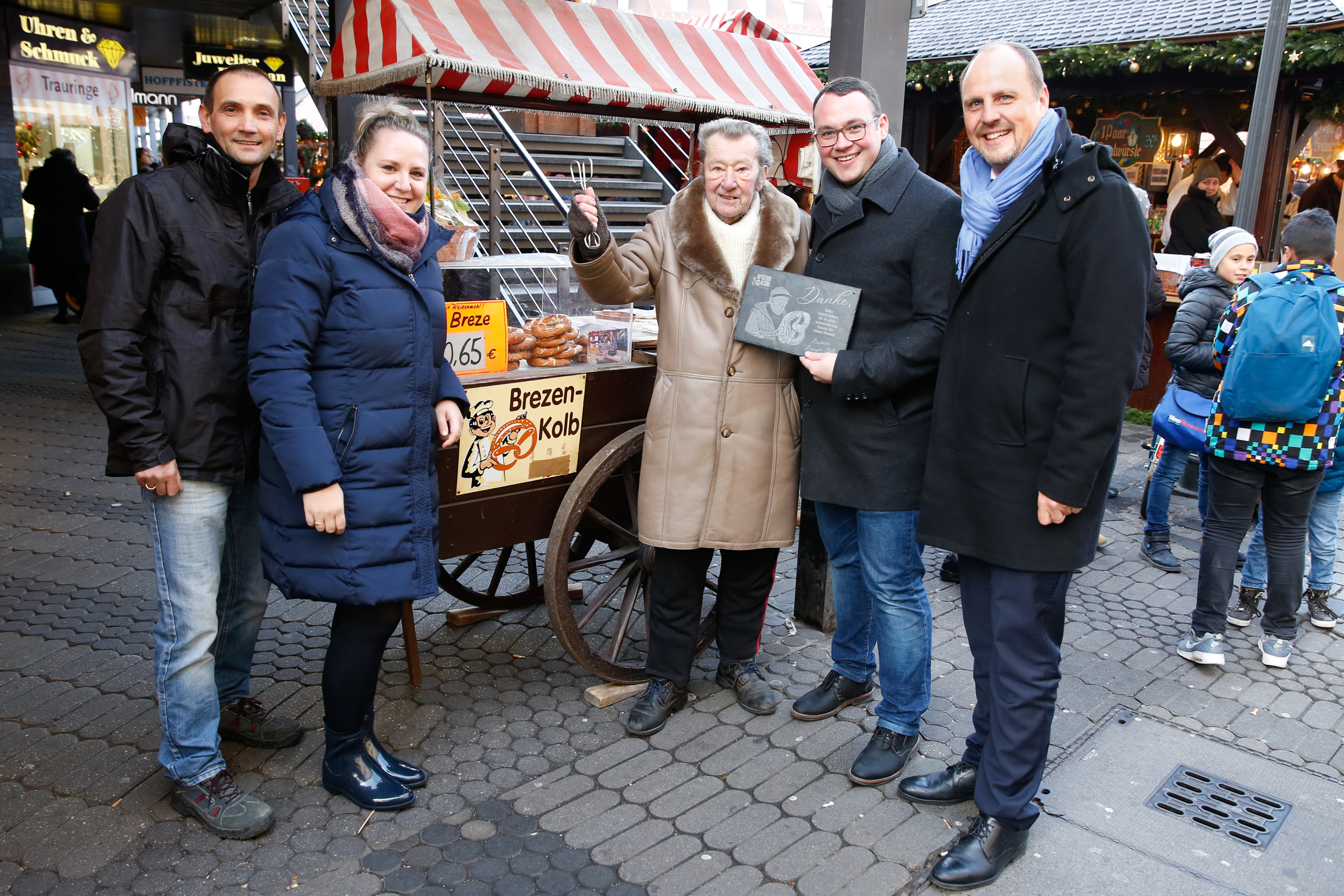 Gunter Seifert war 34 Jahre lang mit seinem mobilen Brezenwagen am Nürnberger Hauptmarkt für das Unternehmen Brezen Kolb tätig. Nun geht der 88-Jährige, der in ganz Nürnberg als der „Brezen-Mann“ bekannt ist, in den Ruhestand und wurde von den Geschäftsführern Jessica und Peter Kolb sowie dem 2. Bürgermeister Christian Vogel feierlich verabschiedet.