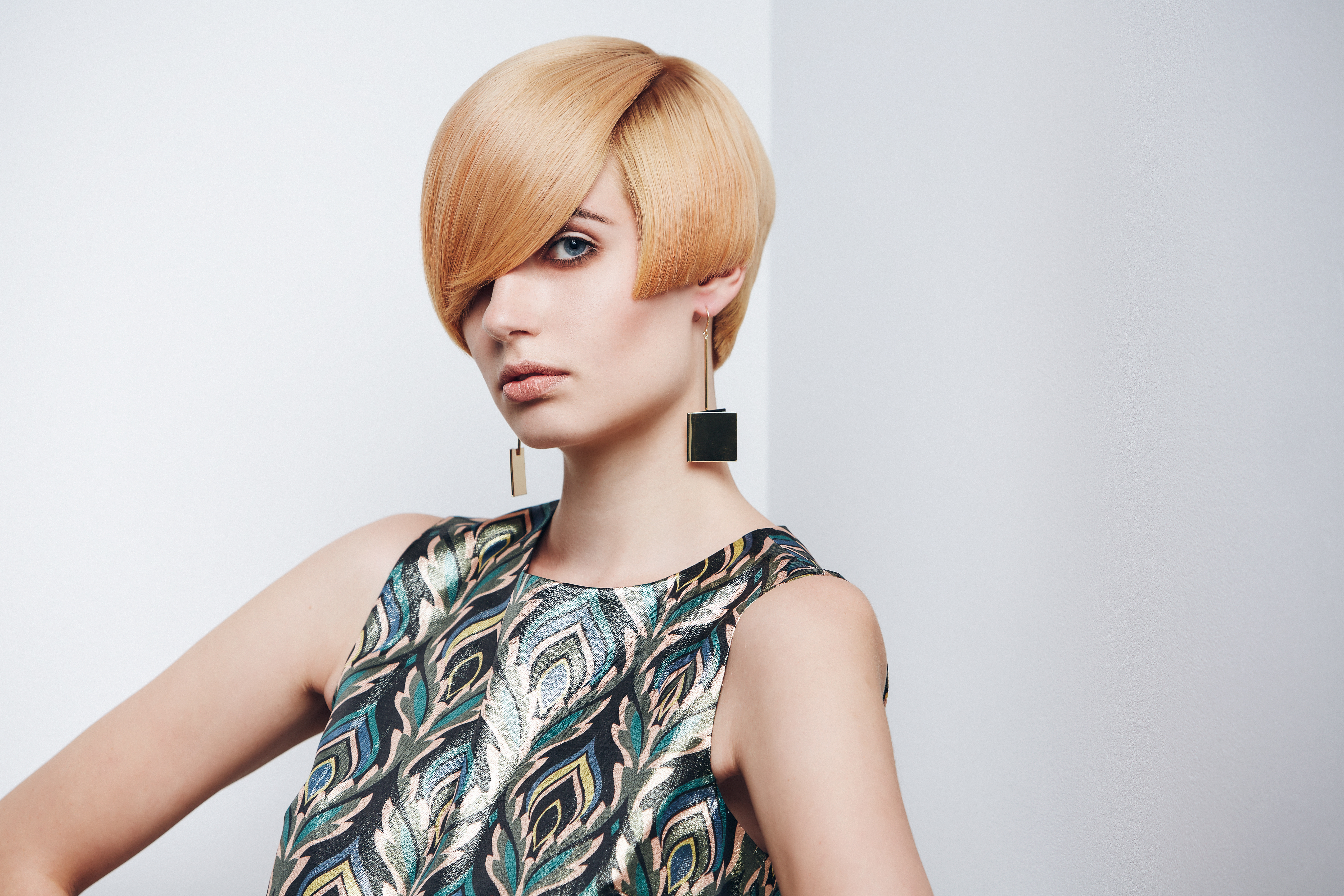 Die grafische Kurzhaarfrisur verleiht der Trägerin durch die harten Konturen, die schmal geschnittene Nackenpartie und das volle Deckhaar ein androgynes und cleanes Aussehen. Die Überlänge des Stirnmotivs betont die Augenpartie und lenkt den Fokus ganz auf das Gesicht.