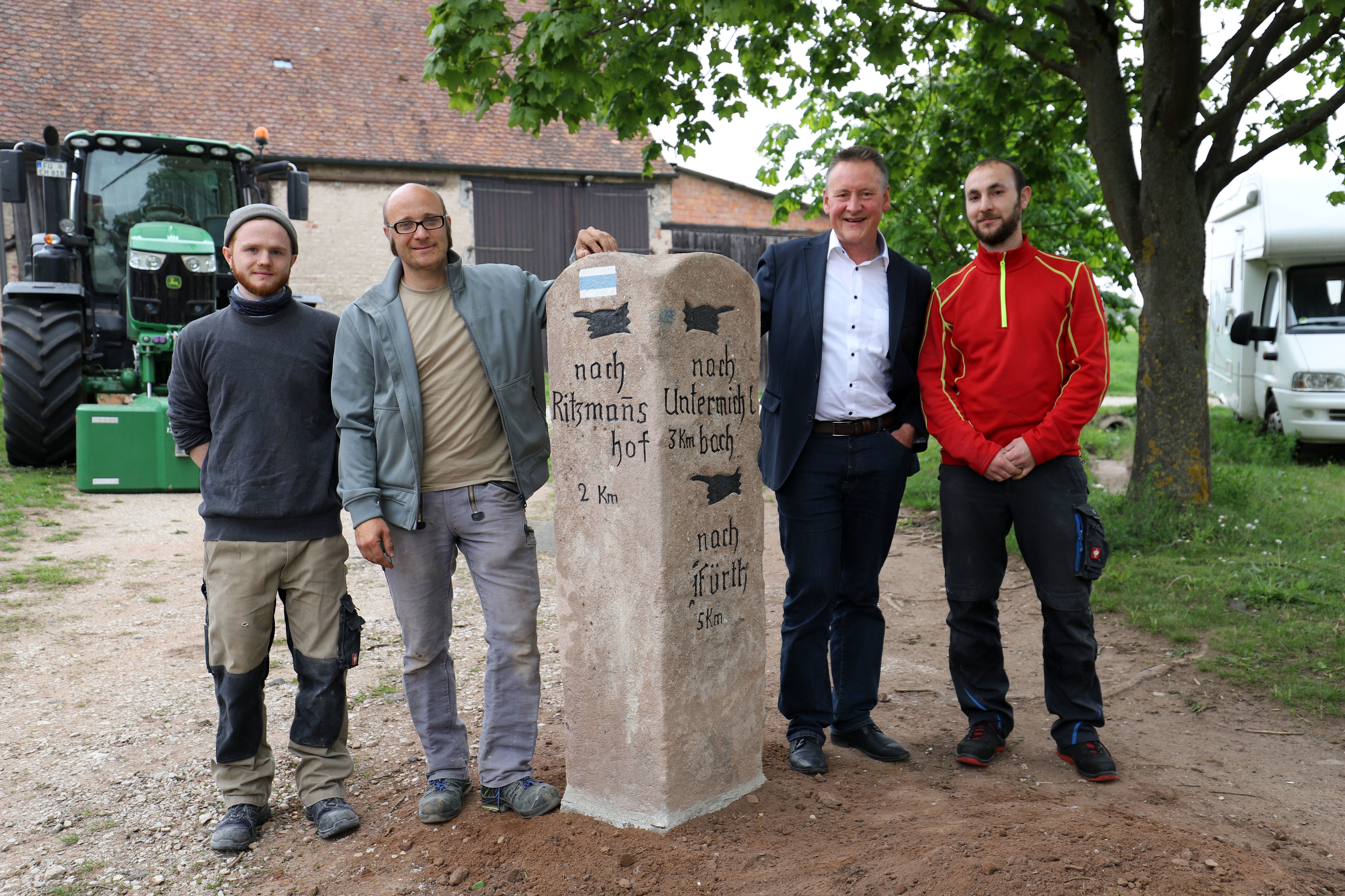 Alexander Müller (re.) hat die stark lädierte Sandsteinsäule in seinem Keller gefunden. Steinmetz Peter Stutzmann (2. v. li.) und sein Azubi (li.) Leon Wilke haben sie restauriert, nun weist sie in Flexdorf wieder den Weg nach Ritzmannshof, Untermichelbach und Fürth – auch sehr zur Freude von OB Jung.