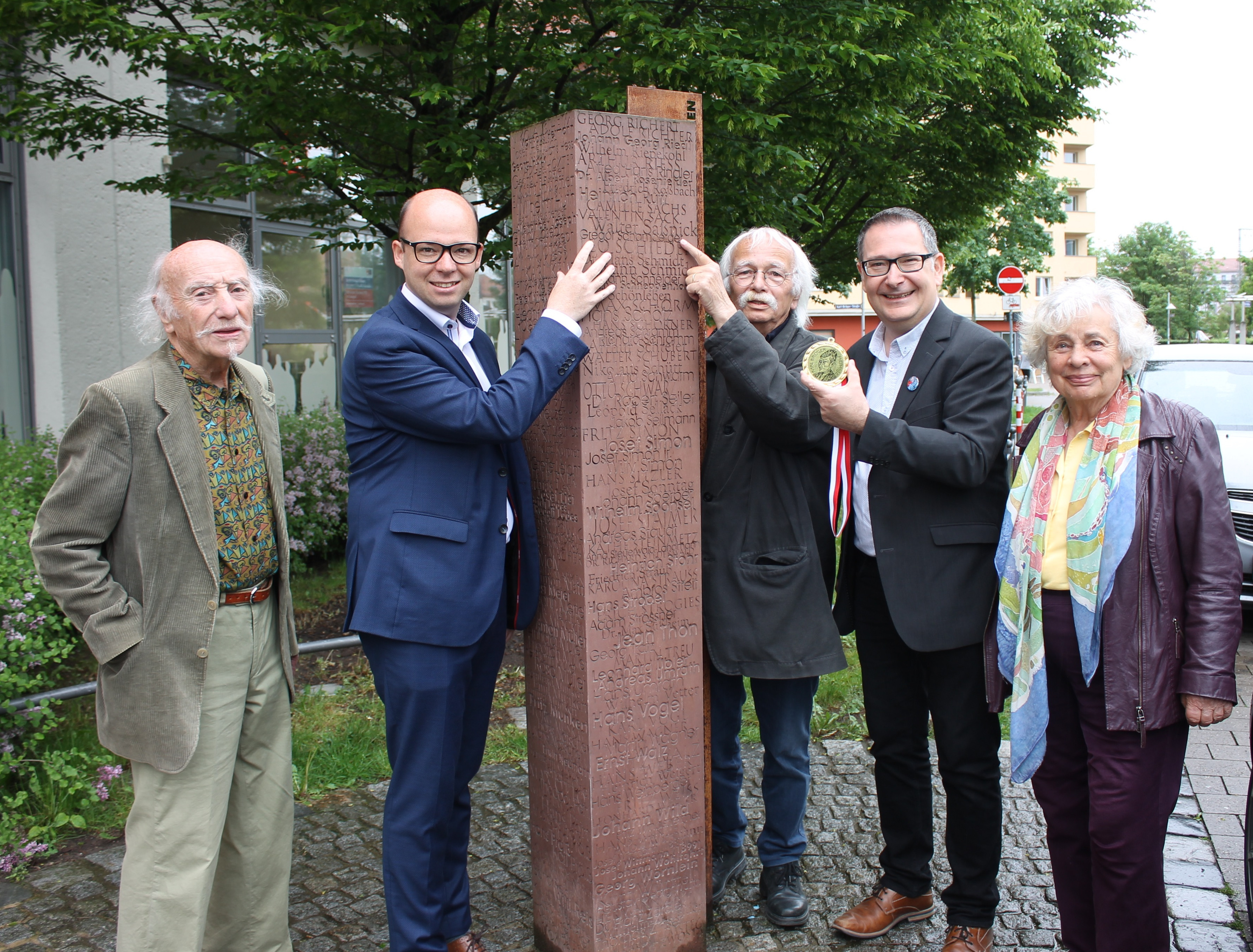 Klaus Schamberger (3.v.r.) und Thorsten Brehm (2.v.l.) deuten an der Erinnerungssäule für im Dritten Reich verfolgte Nürnberger Sozialdemokratinnen und Sozialdemokraten auf den Namen Gregor Schamberger. Michael Ziegler, Alfred Emmerling (l.) und Lilo Seibel-Emmerling freuen sich mit Schamberger, der am 28. Mai die Karl-Bröger-Medaille erhalten soll.