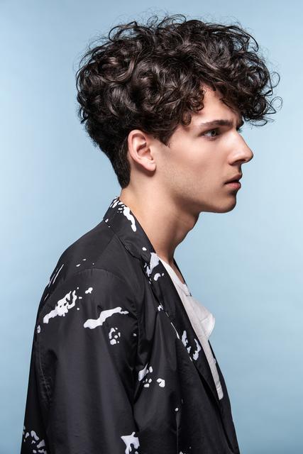 Die neue Quiff-Frisur ist sehr vielfältig. Gerade bei der jüngeren Generation ist der softe, dynamische Look mit Locken und Wellen gefragt. Für ein natürliches Volumen wird die volle Textur am Oberkopf mit Stylingprodukten in Form gebracht. Der typische Rulebreaker. | Foto: © ZV Friseurhandwerk