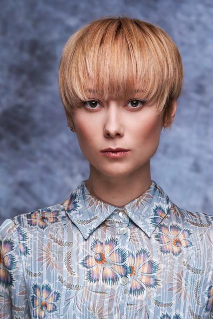 Der Bowl Cut ist mehr als nur ein Haarschnitt – er setzt ein Statement für Offenheit und Stärke. Mit weichen und fedrigen Schnittführungen suggeriert der Look gleichzeitig aber auch eine Leichtigkeit in der Gesamtoptik und wirkt sehr feminin. Das lange Deckhaar fällt weich und rund ins Gesicht und erzeugt viel Bewegung und Volumen. Durch die Aufhellung der Längen und Spitzen des Oberkopfes und der Veredelung im hippen Peach geht mit dem Look die Sonne auf. | Foto: © Zentralverband Friseurhandwerk/Mario Naegler