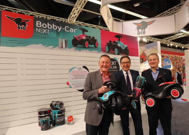 Uwe Weiler (mitte), COO der Simba Dickie Group, präsentiert das Bobby Car Next in zwei neuen Farben. Sie gewannen die Wahl bei einer Social-Media Kampagne.�