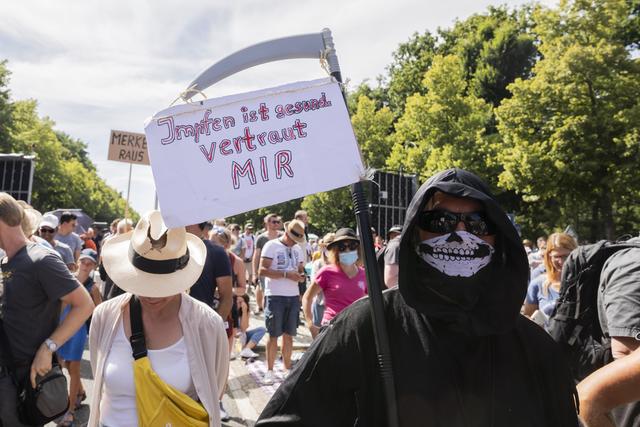 Person im Sensenmann-Kostüm hält ein Schild mit der Aufschrift «Impfen ist gesund, vertraut mir».