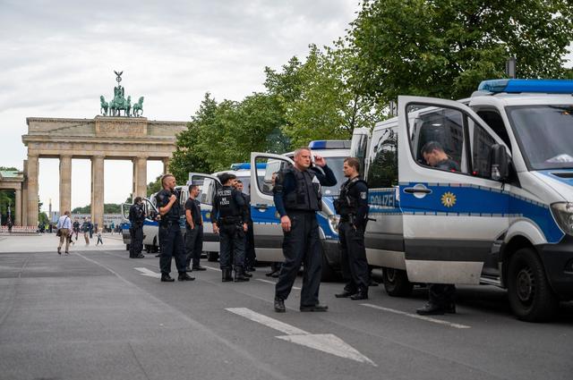 Polizisten stehen am frühen Morgen neben Polizeifahrzeugen vor dem Brandenburger Tor.  | Foto: Christophe Gateau/dpa
