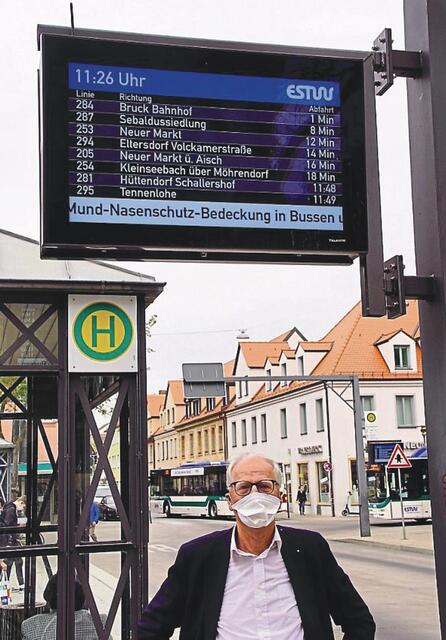 Siegfried Balleis korrekt mit Maske vor einem Fahrtzielanzeiger in Erlangen, der Abfahrtszeiten in Echtzeit angibt.
Foto: © Schweinfurth