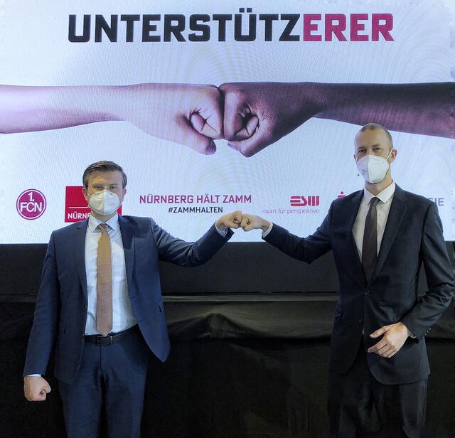 „Fistbump“ zwischen Nürnbergs OB Marcus König (li.) und Niels Rossow, Kaufmännischer Vorstand des 1. FC Nürnberg vorm Motiv „Unterstützerer“. | Foto: Andi Franke/Stadt Nürnberg