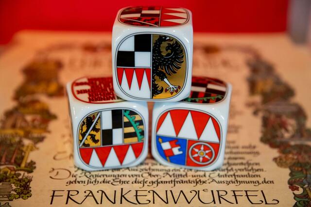 Drei Frankenwürfel aus Porzellan liegen bei der der Verleihung des Frankenwürfels auf einer Urkunde.  | Foto: Daniel Karmann/dpa/Archivbild 