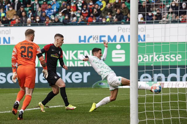 Der Fürther Marco Meyerhöfer (r) schießt neben dem Freiburger Torwart Mark Flekken (l) und Roland Sallai (M) den Ball mit der Fußspitze über das leere Tor. | Foto: Daniel Löb/dpa