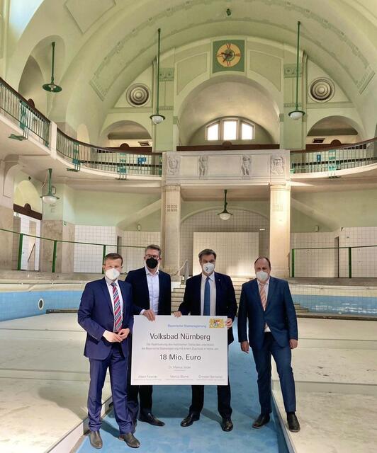 Am Donnerstag, 24. März 2022, nahmen Nürnbergs Oberbürgermeister Marcus König (l.) und Bürgermeister Christian Vogel (r.) aus den Händen des Staatsministers für Wissenschaft und Kunst, Markus Blume, und Bayerns Ministerpräsident Dr. Markus Söder (2.v.r.) in der ehemaligen Schwimmhalle des Volksbades die Förderzusage in Form eines symbolischen Schecks entgegen.

Bildnachweis: Christine Dierenbach / Stadt Nürnberg | Foto: Stadt Nürnberg