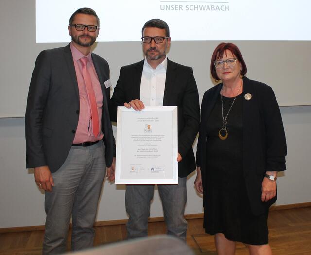 Knut Kosmann (Prokurist der GEWOBAU der Stadt Schwabach GmbH) empfängt die Urkunde von Stephan Stärzl (l.) und Ursula Kaiser-Biburger. | Foto: Victor Schlampp