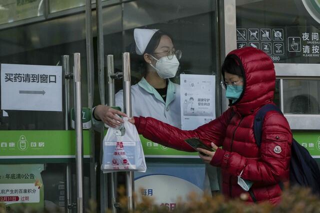 Eine Frau holt in einer Apotheke in Peking COVID-19-Antigen-Kits ab. | Foto: Andy Wong/AP/dpa