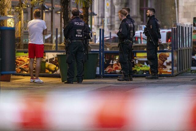 Polizisten stehen in Duisburg bei einem Einsatz neben einem Mann in Sportkleidung, der vor Ort als Zeuge befragt worden sein soll.  | Foto: Christoph Reichwein/dpa