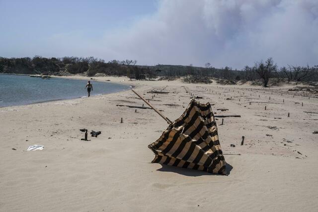 Verbrannte Sonnenliegen und Sonnenschirme an einem Strand auf der Ägäisinsel Rhodos. Foto: Petros Giannakouris/AP/dpa
