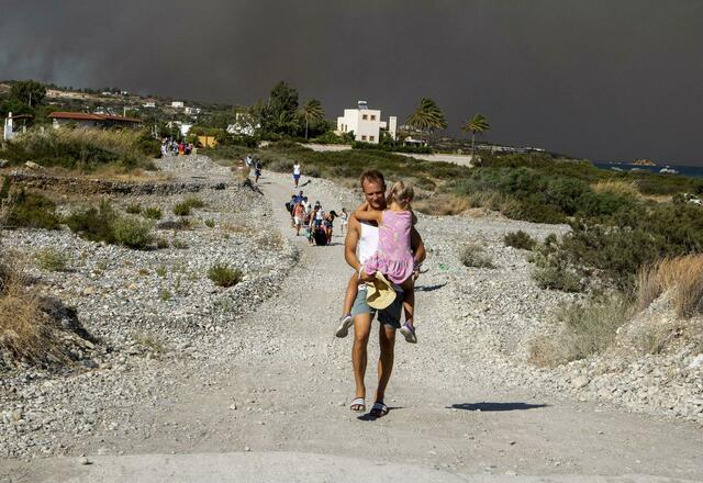 Ein Mann trägt ein Kind, als sie ein Waldbrandgebiet verlassen. | Foto: Lefteris Damianidis/InTime News/AP/dpa