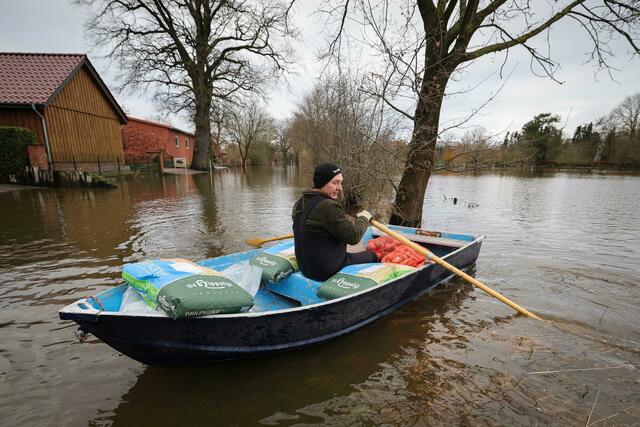 Ein Anwohner bringt mit einem kleinen Ruderboot Futter für seine Tiere über eine überschwemmte Straße in Hagen-Grinden zu seinem Hof.  | Foto: Christian Charisius/dpa