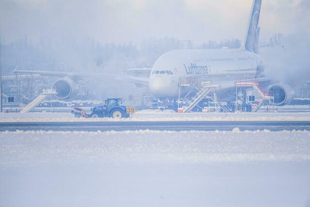Ein Schneeräumer fährt im Schneetreiben auf dem Flughafen vor einer Maschine entlang. | Foto: Jason Tschepljakow/dpa