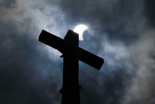 Wolken lösen sich auf und geben über dem Kreuz eines Kirchturms in Manor (Texas) den Blick auf die beginnende Sonnenfinsternis frei.  | Foto:  Charles Rex Arbogast/AP