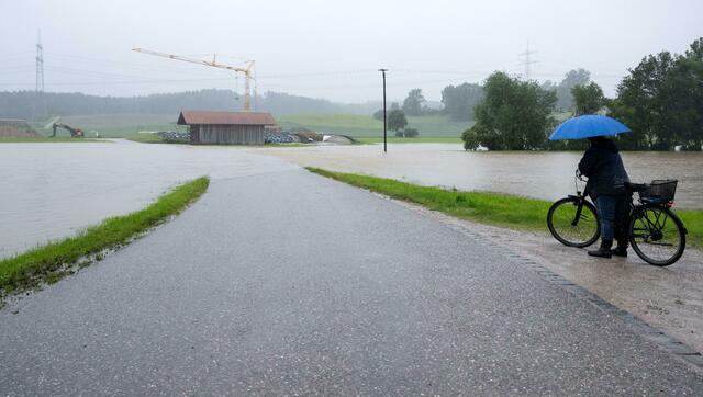 Eine Frau steht mit ihrem Fahrrad an einer überspülten Straße. Mit der Welle verlagere sich der Schwerpunkt stromabwärts - von Schwaben Richtung Niederbayern und Oberpfalz. Unter anderem in Neuburg, Kelheim, Regensburg, Straubing könnten betroffen sein, die Scheitelwelle wird aber voraussichtlich erst Anfang der Woche durchfließen.  | Foto: Sven Hoppe/dpa