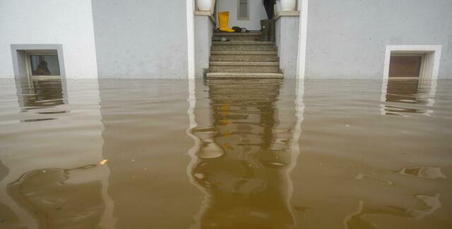 Im Treppenaufgang eines Hauses, dessen Untergeschoss voll Wasser ist, stehen Gummistiefel.  | Foto:  Stefan Puchner/dpa