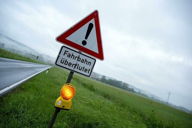 Ein Schild warnt vor Hochwasser, die Straße dahinter ist überflutet.  | Foto: Pia Bayer/dpa