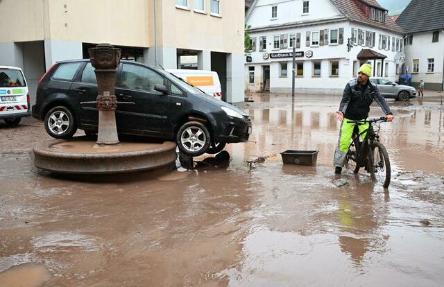 Auf einem Brunnen in Rudersberg steht ein durch ein Hochwasser weggespültes Auto.  | Foto: Bernd Weißbrod/dpa