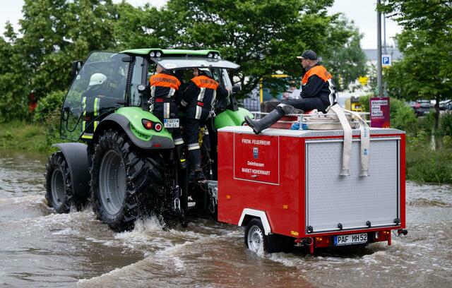 Feuerwehrleute fahren in Reichertshofen über eine überflutete Straße.  | Foto: Sven Hoppe/dpa
