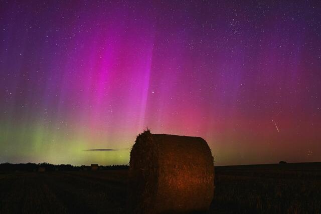 Nordlichter am Himmel, während eine Sternschnuppe über einem Strohballen am Himmel verglüht. | Foto: Georg Moritz/dpa