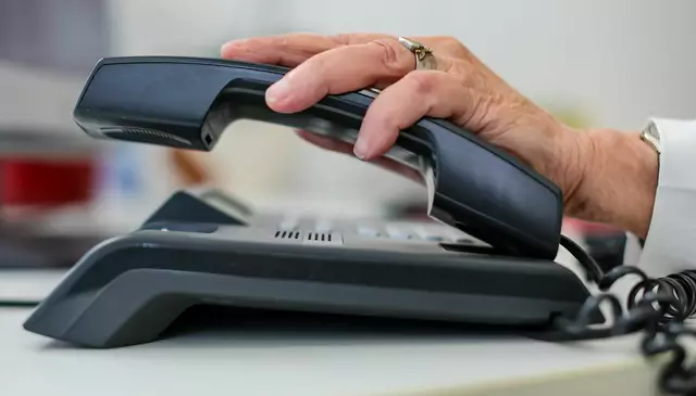 Eine Frau nimmt einen Telefonhörer in die Hand. | Foto: Jan Woitas/dpa (Symbolfoto)